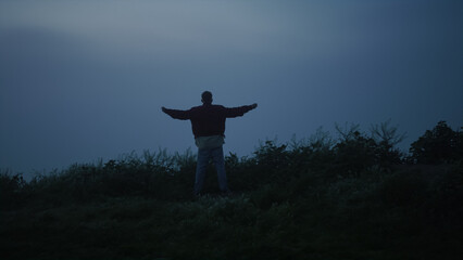 Lonely guy walking in misty field. Back view man raising hands in air