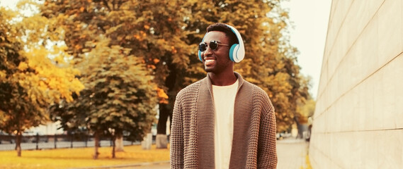 Portrait of happy smiling young african man in headphones listening to music wearing brown knitted...