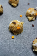 Close-up of Halloween cookies with spooky funfetti confetti candy sprinkles shaped like ghosts, bats and pumpkins on baking sheet, raw sugar cookie dough balls before baking - 532297451