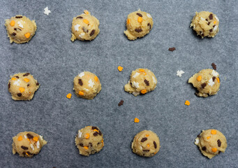 Close-up of Halloween cookies with spooky funfetti confetti candy sprinkles shaped like ghosts, bats and pumpkins on baking sheet, raw sugar cookie dough balls before baking - 532297462