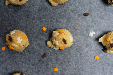 Close-up of Halloween cookies with spooky funfetti confetti candy sprinkles shaped like ghosts, bats and pumpkins on baking sheet, raw sugar cookie dough balls before baking - 532297468