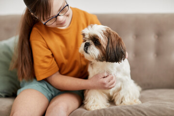 Portrait of cute girl with Down syndrome playing with small dog while sitting on couch together,...