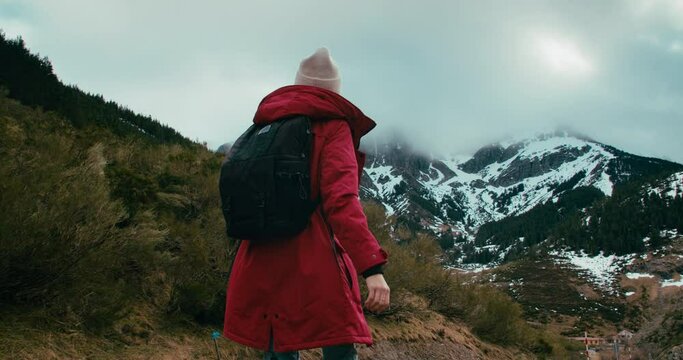 Hiker woman walk on tourist trail surrounded by beautiful mountain landscape on winter weekend trip. Female traveler in red jacket and backpack hike on travel adventure. Active lifestyle and journey