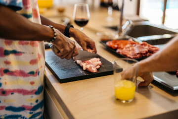 hands of a black man cutting pork ribs on a board