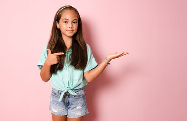 cheerful, happy girl child points to the side on a pink background, copying the place for the...