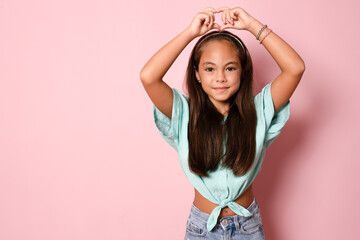 Beautiful cute little girl making heart figure with fingers standing isolated over pink background.