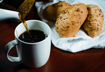 coffee falling into a white porcelain cup with bread next to it on a white handkerchief
