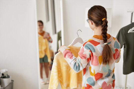 Back view at teenage girl with Down syndrome choosing clothes and looking at mirror at home, copy space