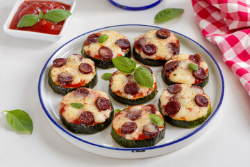Zucchini Pizza Bites. Grilled zucchini slices with tomato sause, sausage, basil and melted mozzarella cheese served on a white plate.