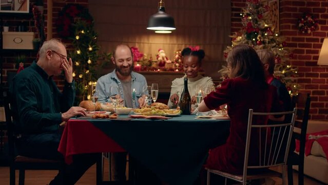 Joyful diverse people enjoying traditional home cooked food while sitting at Christmas dinner table. Happy family at home celebrating winter holiday together while being positive and peaceful.
