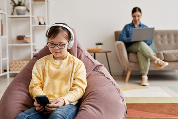 Portrait of teen girl with Down syndrome playing mobile games at home with parent supervision, copy...
