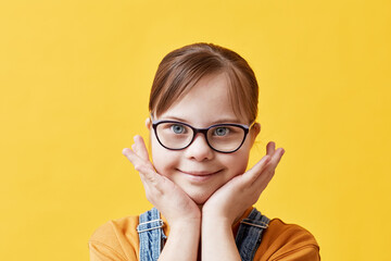 Closeup portrait of cute girl with Down syndrome looking at camera against yellow background in...