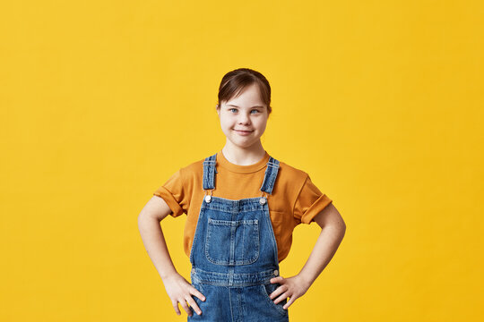 Waist up portrait of cute girl with Down syndrome looking at camera against yellow background in studio