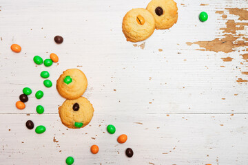 Homemade sugar cookies with chocolate candies in Halloween treats colors orange and green on baking sheet on white background, easy and fun biscuit baking recipe for kids for trick or treating sweets - 532309428