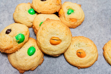 Typical American sugar cookies with chocolate covered candies in Halloween treats colors orange and green on baking sheet, easy and fun biscuit baking recipe for kids for trick or treating sweets - 532309435