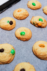 Typical American sugar cookies with chocolate candies in Halloween treats colors orange and green on baking sheet, easy and fun biscuit recipe for kids for trick or treating sweets - 532309475
