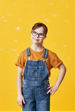 Vertical portrait of cute girl with Down syndrome looking at camera against yellow background in studio