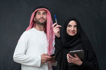 Young muslim business couple in fashionable hijab dress using smartphone and tablet in front of...