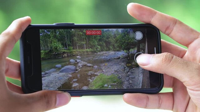A Young Man's Hand Taking a Video of a River With His Smartphone in the Nature