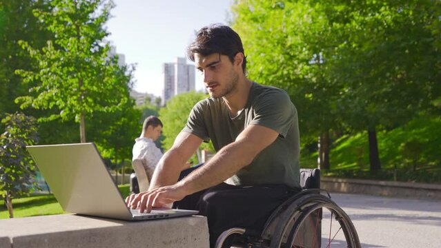 Young physically disabled working with laptop outdoors.
Disabled young man working with laptop and earning, rejoicing.
