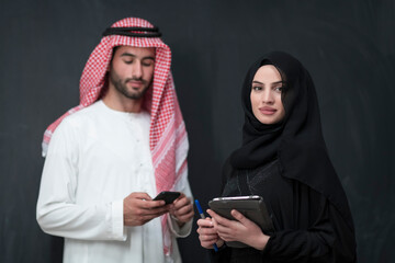 Young muslim business couple in fashionable hijab dress using smartphone and tablet in front of...