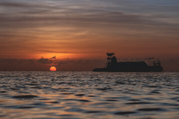 Beautiful sunset on the beach with a silhouette of a boat. © Paniagua 