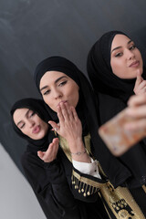 Group of young beautiful muslim women in fashionable dress with hijab using smartphone while taking...
