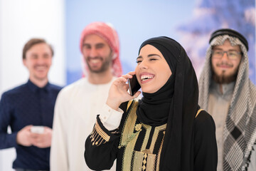 Group portrait of young Muslim people women in fashionable hijab dress with three Arabian men using smartphones at modern bright home