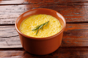 Polenta in ceramic bowl on rustic wooden table. Cream of corn or mamaliga