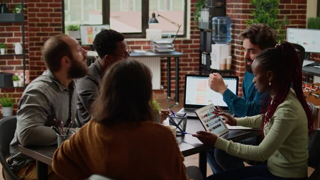 Diverse team of colleagues working on business partnership, creating presentation report with charts data on documents and laptop. People doing teamwork collaboration in boardroom meeting.