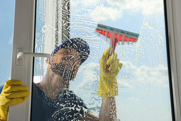 Man cleaning glass with squeegee indoors, view from inside