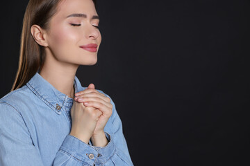 Woman with clasped hands praying on black background, space for text