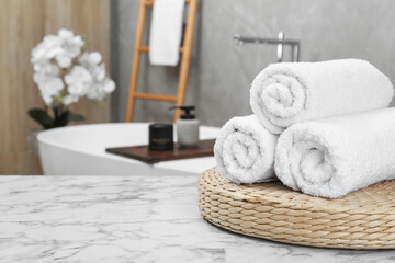 Rolled bath towels on white marble table in bathroom, space for text