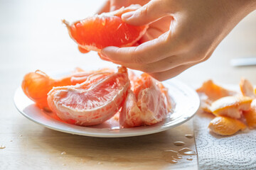 Citrus fruit.Womans hands peeling a grapefruit.Fresh and juicy grapefruit.Splashes and drops of grapefruit juice.Fruit for breakfast. breakfast preparation 