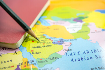 selected focus Saudi Arabia on a world map with book and pencil.