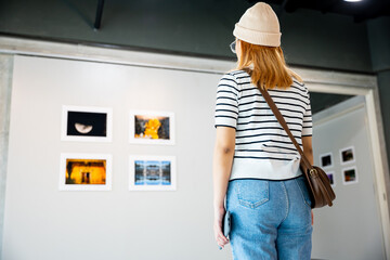 Asian woman standing she looking art gallery in front of colorful framed paintings pictures on...