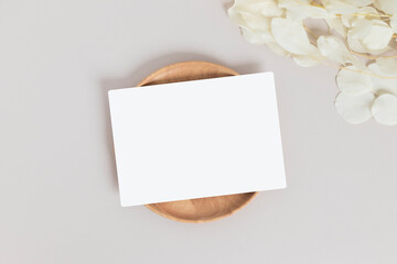 Greeting card or invitation card with white dry flower leaves on wood plate or tray in beige background