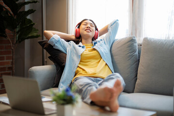 Happy asian woman listening to music while leaing back on couch.