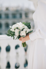 The bride in a white dress holds a delicate wedding bouquet in her hands.