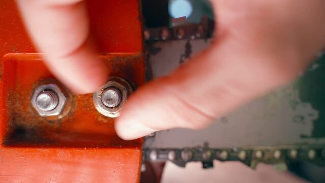 Tightening the nut securing the casing of the chainsaw tire close-up. Repair and maintenance of an old orange chainsaw. Close-up hand tightening a nut on a stud with fingers