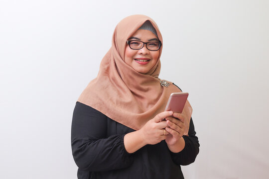 Portrait of cheerful Asian woman with hijab, holding mobile phone and feeling excited. Advertising concept. Isolated image on white background