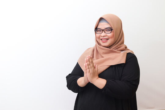 Portrait of cheerful Asian woman with hijab, showing apologize and welcome hand gesture. Advertising concept. Isolated image on pink background