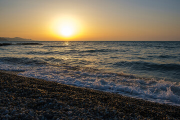 Gorgeous sea sunset landscape. MIrror reflection of dawn on wet pebble. Golden sunlight over sea waves. Close up of tide and sea pebble coast
