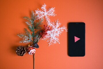 再生マークのついたスマートフォンとクリスマスの装飾と赤背景の写真