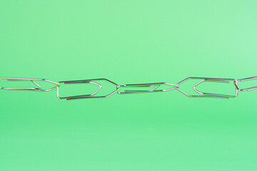 Paper clips connected to each other on green background.