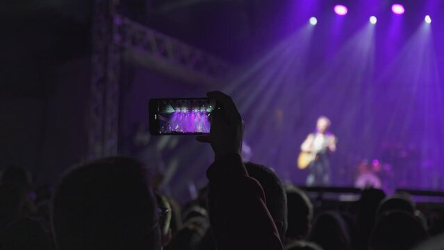 Mobile phone in hands and live performance or concert, flashing lights and blurry background