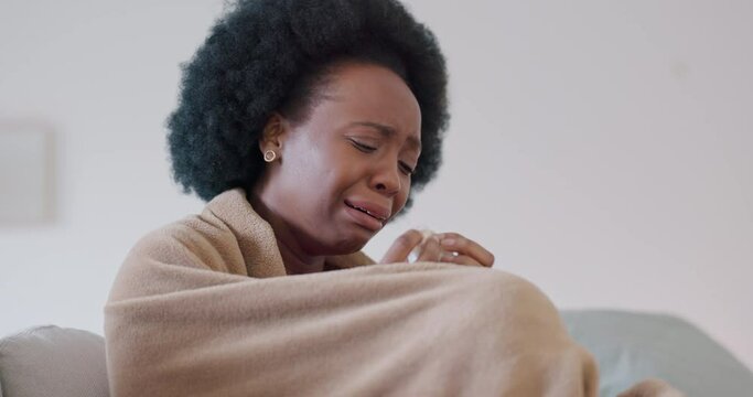 Sad crying black woman with depression at home on couch, sofa or living room mourning the loss of a loved one. Anxiety, stress and tears of African female with poor mental health after abuse