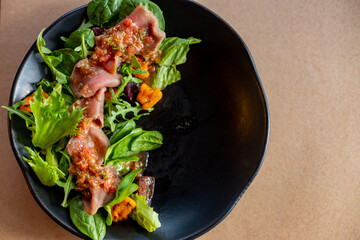 Delicious salad with spinach, tangerine, salmon with citrus dressing on a black plate, top view.Mediterranean salmon salad bowl.Fresh salad on green leaves.copy space