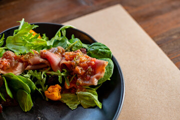 Delicious salad with spinach, tangerine, salmon with citrus dressing on a black plate, side view.Mediterranean salmon salad bowl.Fresh salad on green leaves.copy space