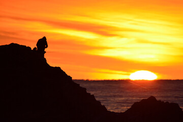 fishermen in a sunrise on the rocks in the sea